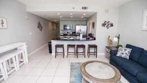 A modern kitchen with a central island, bar stools, a blue sofa, and a coffee table. - Low Floor, beautiful ocean views, seasonal beach chair service. No elevator wait (Panama City Beach)