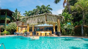 A pool area with a thatched-roof structure, palm trees, and a clear blue pool. - Marea Brava Hotel & Villas (Jacó)