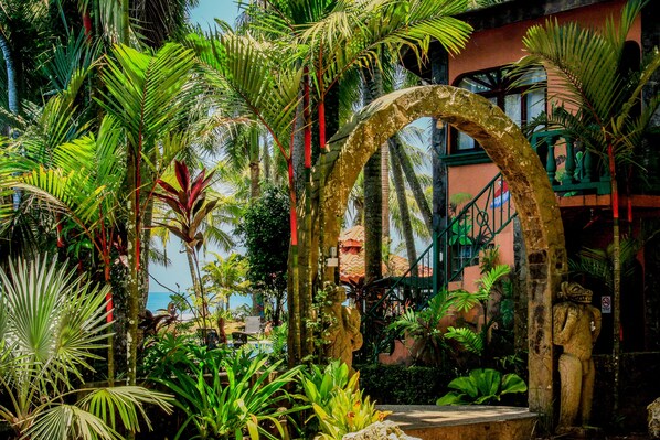 A lush garden with tropical plants and a stone archway.