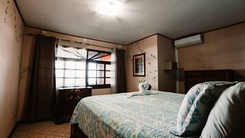 Un dormitorio con cama, ventana con cortinas, aire acondicionado de pared y un cuadro enmarcado.