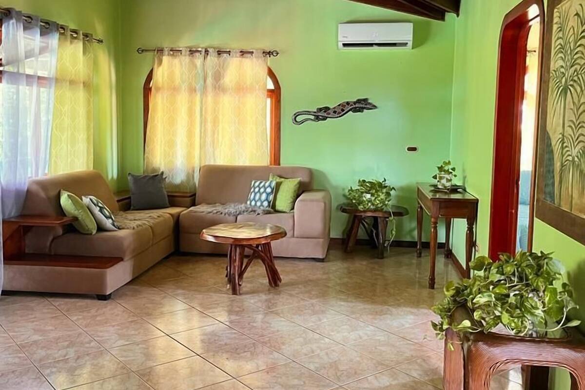 A living room with a wooden ceiling, green walls, a sofa set, a coffee table, and potted plants.