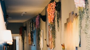A hallway with a light fixture on the left, a door at the end, and wall-mounted decorations including flowers and framed pictures. - Cati Hotel Boutique Plus (Cesme)