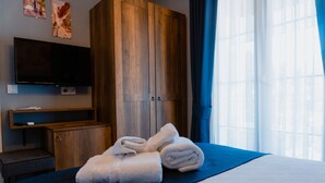 A hotel room with a bed, a TV mounted on the wall, wooden wardrobe, and a window with curtains. - Cati Hotel Boutique Plus (Cesme)