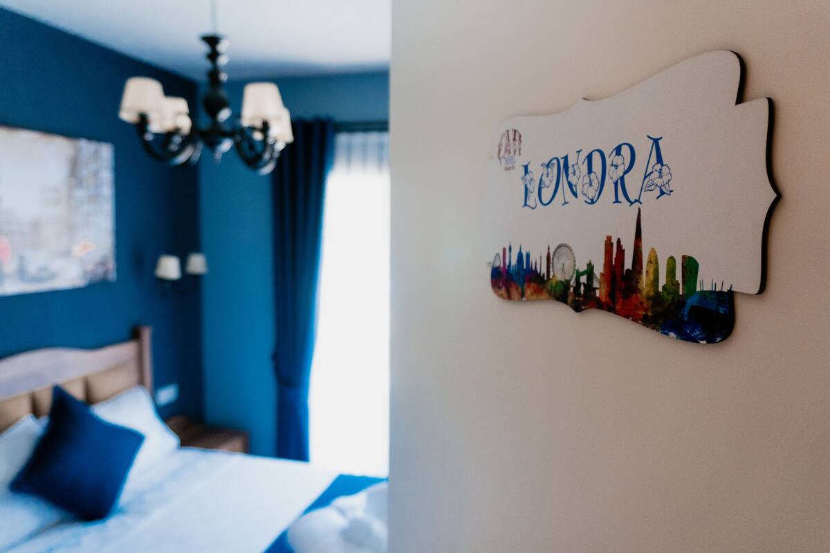 Un dormitorio con cama, almohadas y un candelabro. Hay una decoración en la pared con el nombre "LONORA" y un horizonte urbano.