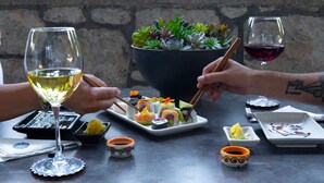 A table with sushi, a bowl of green plants, and two glasses of wine. - Cati Hotel Boutique Plus (Cesme)