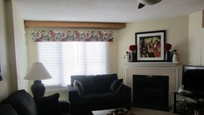 A living room with a sofa, a coffee table, a fireplace, a television, and a window with blinds. - 2BR/BA Silver Creek, Ski-in/out, Indoor/Outdoor Pool & Hot Tub (Snowshoe)