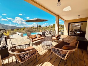 Une terrasse en bois avec des meubles en osier, une piscine et une vue sur les montagnes.