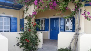A building with a yellow facade, blue doors, and a covered entrance with a flowering vine. - Santorious Cavehouse (Santorini)