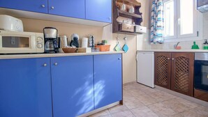 A kitchen with blue cabinets, a microwave, a coffee maker, and a small refrigerator. - Santorious Cavehouse (Santorini)