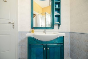 A bathroom with a white door, a sink with a mirror above it, and a teal vanity. - Santorious Cavehouse (Santorini)