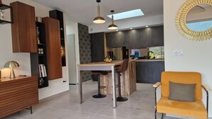 Een moderne keuken met donkere kastjes, een houten kookeiland en een bar. Er staat een gele stoel en een ronde spiegel met een zonachtige inleg op de muur.