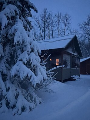 Une cabane au toit en pente, entourée d’arbres couverts de neige.