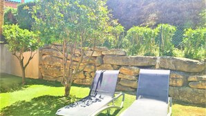 Two lounge chairs in a garden with a stone wall and trees in the background.