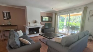 A living room with two grey sofas, a coffee table, a fireplace, a television, and a sliding glass door leading to a patio.