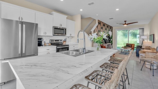 A modern kitchen with white cabinets, stainless steel appliances, a marble countertop, and a bar area with wicker chairs. - *New Construction Luxury Townhome 3mi to downtown* (saint augustine)