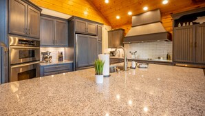 A kitchen with granite countertops, stainless steel appliances, and wooden ceiling. - Luxurious Cabin / Theater / Game Room / Hot Tub / Large Deck / Panoramic View (Sevierville)