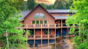 A two-story log cabin with a balcony and a large window. - Luxurious Cabin / Theater / Game Room / Hot Tub / Large Deck / Panoramic View (Sevierville)
