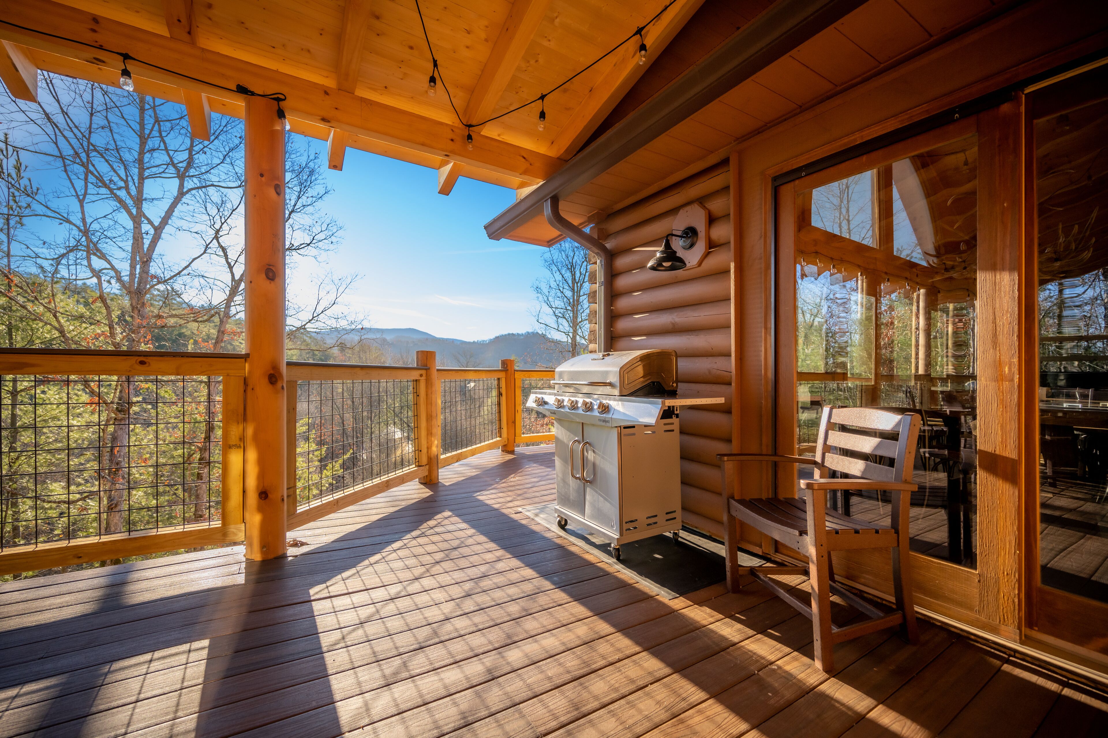 A wooden deck with a grill and seating area, overlooking a mountainous landscape.