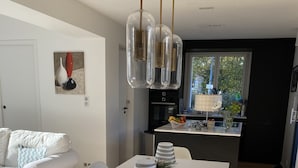 Cocina moderna con comedor, que incluye una mesa blanca, sillas e iluminación colgante con pantallas de vidrio transparente.