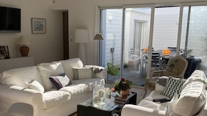 Un salón moderno con muebles blancos, una mesa de centro de vidrio y vistas al exterior a través de grandes puertas correderas de cristal.