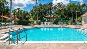 A swimming pool surrounded by palm trees and lounge chairs, with a gazebo in the background.