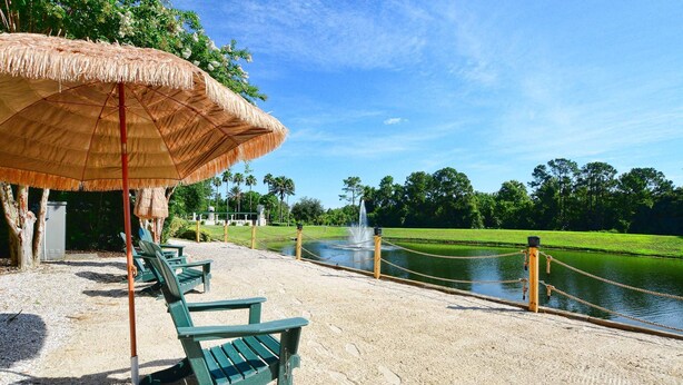 A sandy beach area with a thatched umbrella, green lounge chairs, and a water feature.