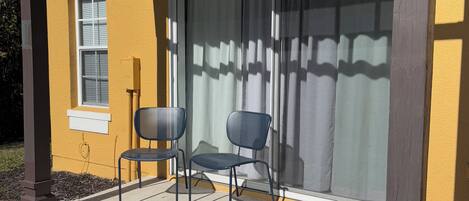 Un patio cubierto con dos sillas y una ventana con persianas.