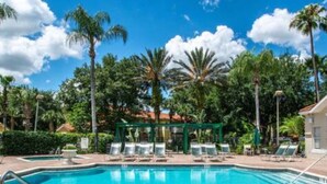 A swimming pool surrounded by palm trees and lounge chairs, with a gazebo in the background. - 4 miles to Disney No Pet Fee! Low cleaning fee! Pools, hot tubs, Tiki Bar etc! (Kissimmee)