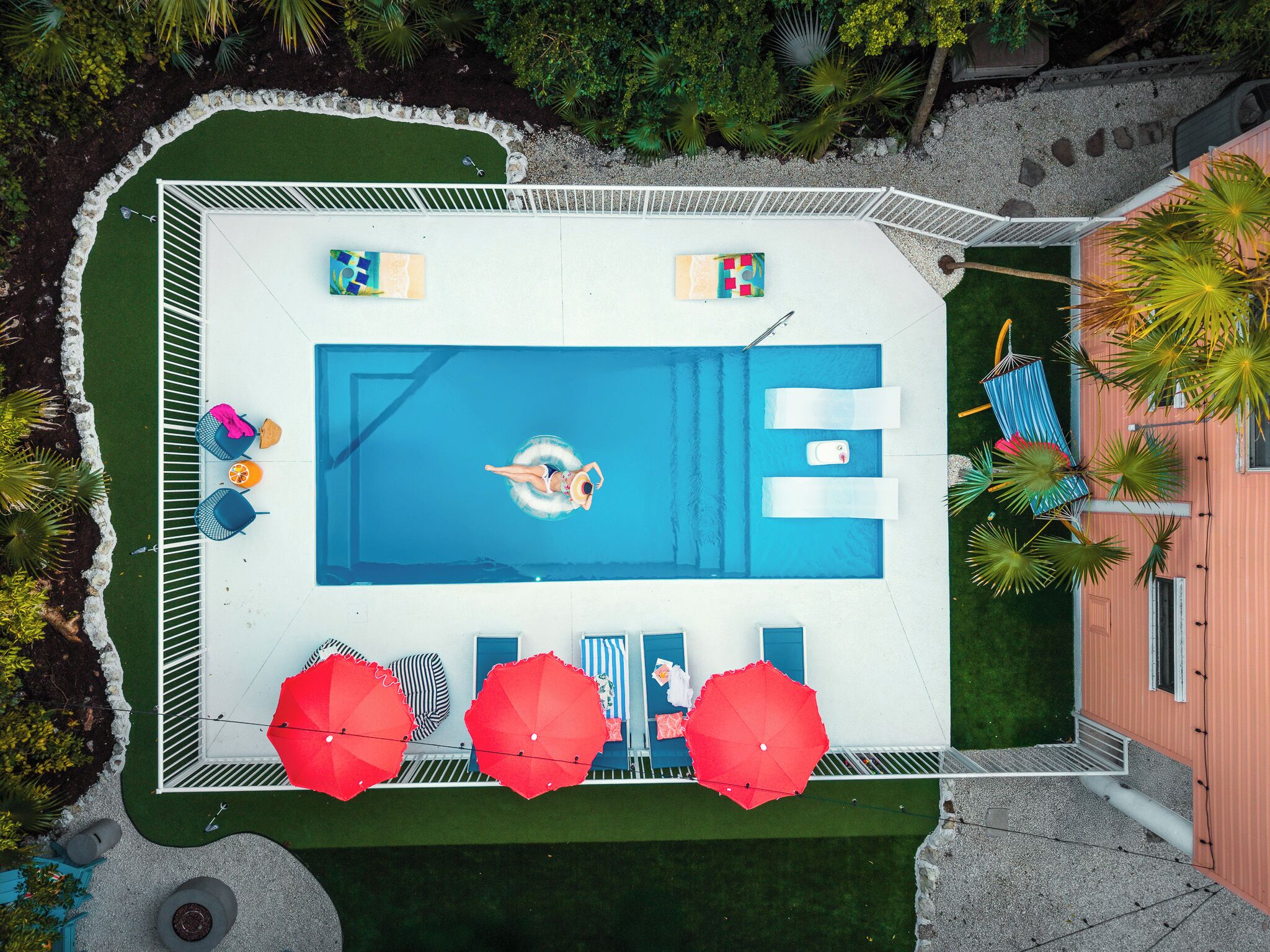 An aerial view of a swimming pool with lounge chairs, umbrellas, and a person swimming.