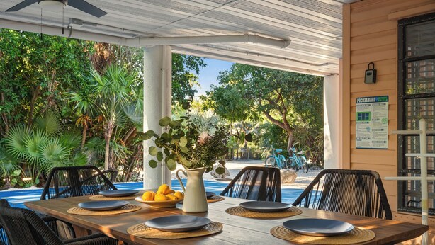 An outdoor dining area with a wooden table, black wicker chairs, and a view of a pool and greenery. - NEW!The Hideaway~Pool~Pickleball~Putt-Putt~Kayaks! (Marathon)