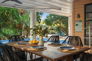 An outdoor dining area with a wooden table, black wicker chairs, and a view of a pool and greenery. - The Hideaway Pool! Pickleball! Putt-Putt! Kayak! Bikes! (Marathon)