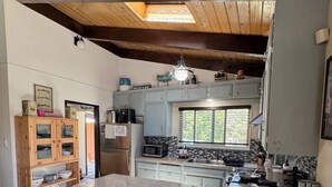Una cocina con una isla grande, taburetes de bar, un armario de madera y un ventanal.