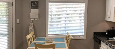 A dining area with a table set for four, a window with blinds, and a kitchen area with cabinets and a sink.