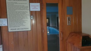 Une porte en bois avec une pancarte indiquant les règles d’utilisation du jacuzzi et du sauna, un panneau de vidéosurveillance et un panneau de commande.