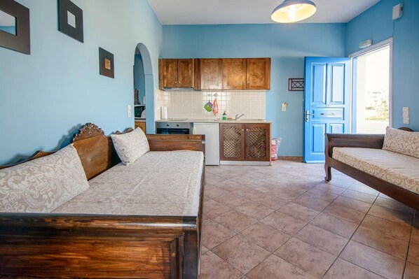 A compact room with a bed, a sofa, a kitchenette, and a door leading outside.