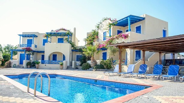 Une piscine avec une terrasse carrelée, un espace détente couvert équipé de chaises longues, et un bâtiment aux accents bleus et aux décorations florales.