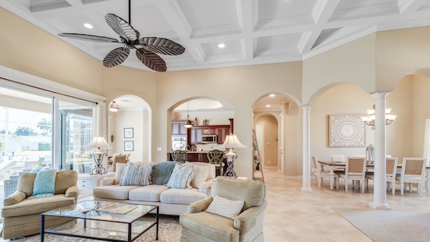 Un salon spacieux doté d’un grand ventilateur de plafond, d’une table basse en verre et d’un ensemble de canapés de couleur beige.