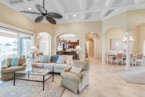 A spacious living room with a high ceiling fan, a glass coffee table, and a beige sofa set. - Blue Anchor Villa luxury 4 bedroom Home  (Marco Island)