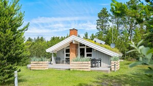 Une petite cabane à un seul étage, dotée d’un toit en pente, d’une cheminée en briques et d’une terrasse avec des meubles d’extérieur.