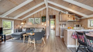 Un loft spacieux avec de hauts plafonds, des poutres apparentes, un coin salon confortable avec un canapé et une table basse, une cuisine avec des meubles en bois et un coin repas avec une table et des chaises.