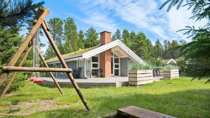 Une maison avec un toit en pente, une cheminée en briques et une terrasse aménagée avec du mobilier d’extérieur.
