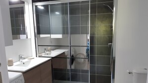 A modern bathroom with a glass shower enclosure, a sink, and a toilet. - Apartment T2 ANGLET (Anglet)