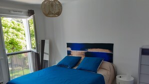 A modern bedroom with a large bed, a view of greenery outside, and a white bedside table. - Apartment T2 ANGLET (Anglet)