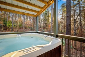 Un jacuzzi en un espacio exterior cubierto con vistas a un bosque.