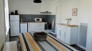 A compact kitchen with white cabinets, a microwave, a sink, and a stove. There's a dining table with a striped tablecloth and a basket on it. - Detached house near beach and shops (Barbâtre)