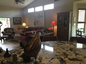 Uma sala de estar ampla com uma grande mesa de madeira, um sofá vermelho e uma escultura decorativa de um galo de metal.