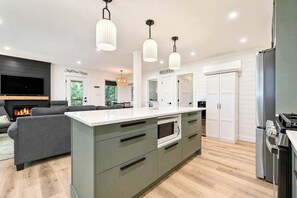 Une cuisine moderne dotée d’un îlot central, d’appareils électroménagers intégrés et de luminaires suspendus.