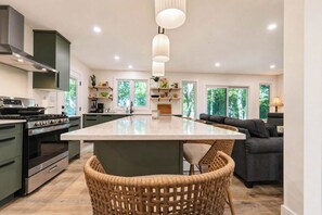 A modern kitchen with a central island, built-in appliances, and a dining area with wicker chairs. - Lakefront Haven, Brand new! Beachfront escape! (Bayfield)