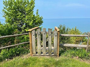 Une porte en bois avec une poignée en métal, entourée de verdure et donnant sur une étendue d’eau.