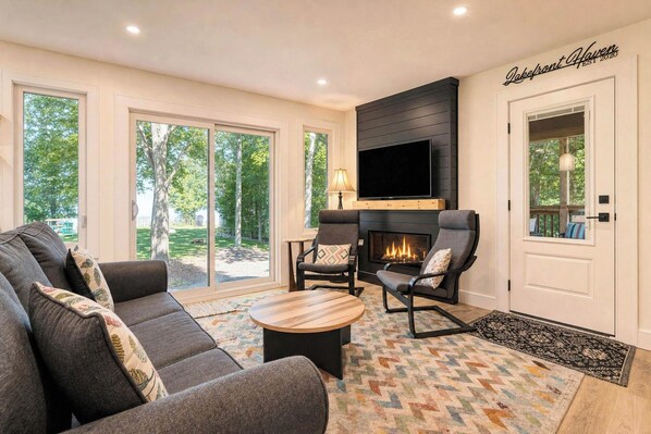 A modern living room with a fireplace, comfortable seating, and large windows offering a view of the outdoors.